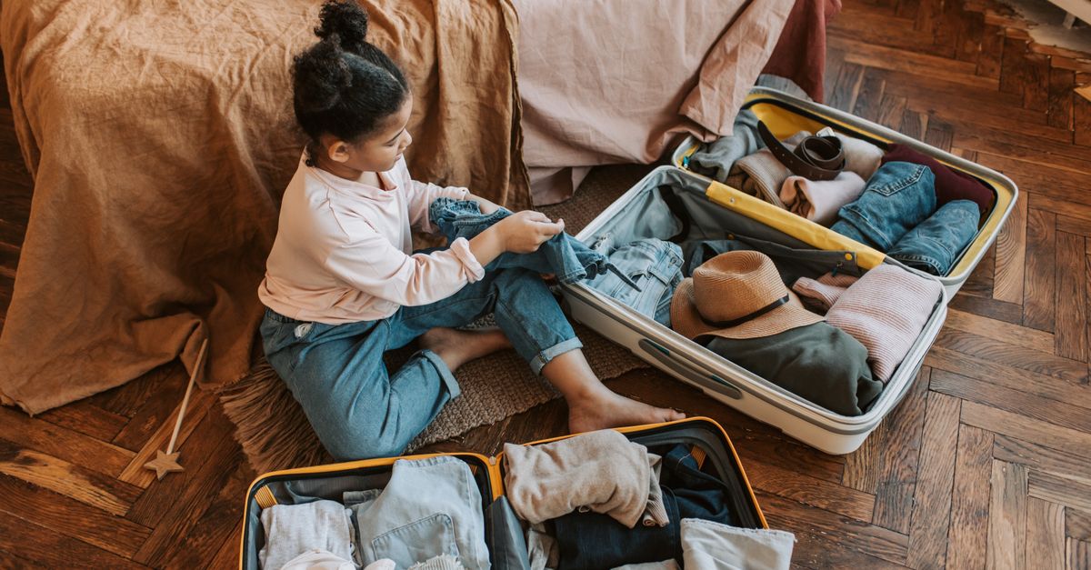 Young child sitting on bed packing a suitcase for an upcoming family vacation.